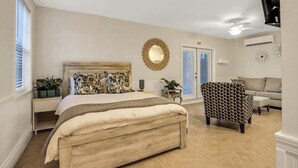 A bedroom with a wooden bed, a patterned armchair, a round mirror, and a door marked "EXIT". - Historic Downtown Casita A (St. Augustine)