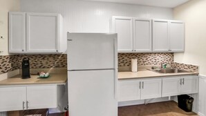 A modern kitchen with white cabinets, a black coffee maker, and a stainless steel sink. - Historic Downtown Casita A (St. Augustine)