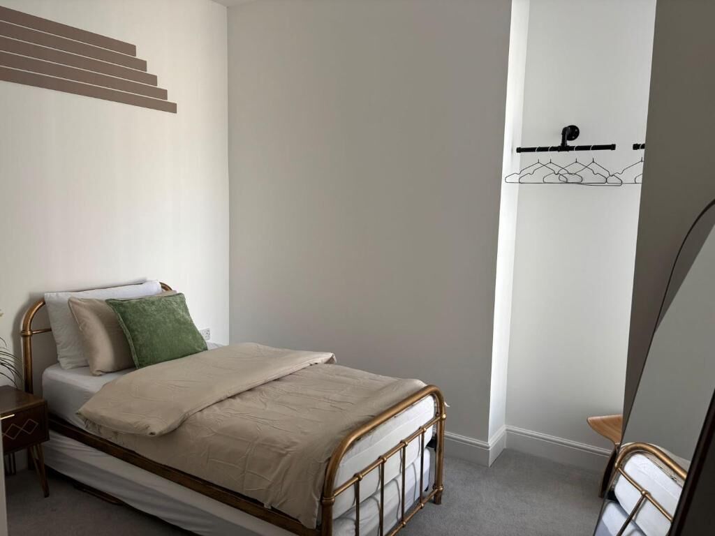 A bedroom with a bed, a nightstand, a chair, and a coat rack.