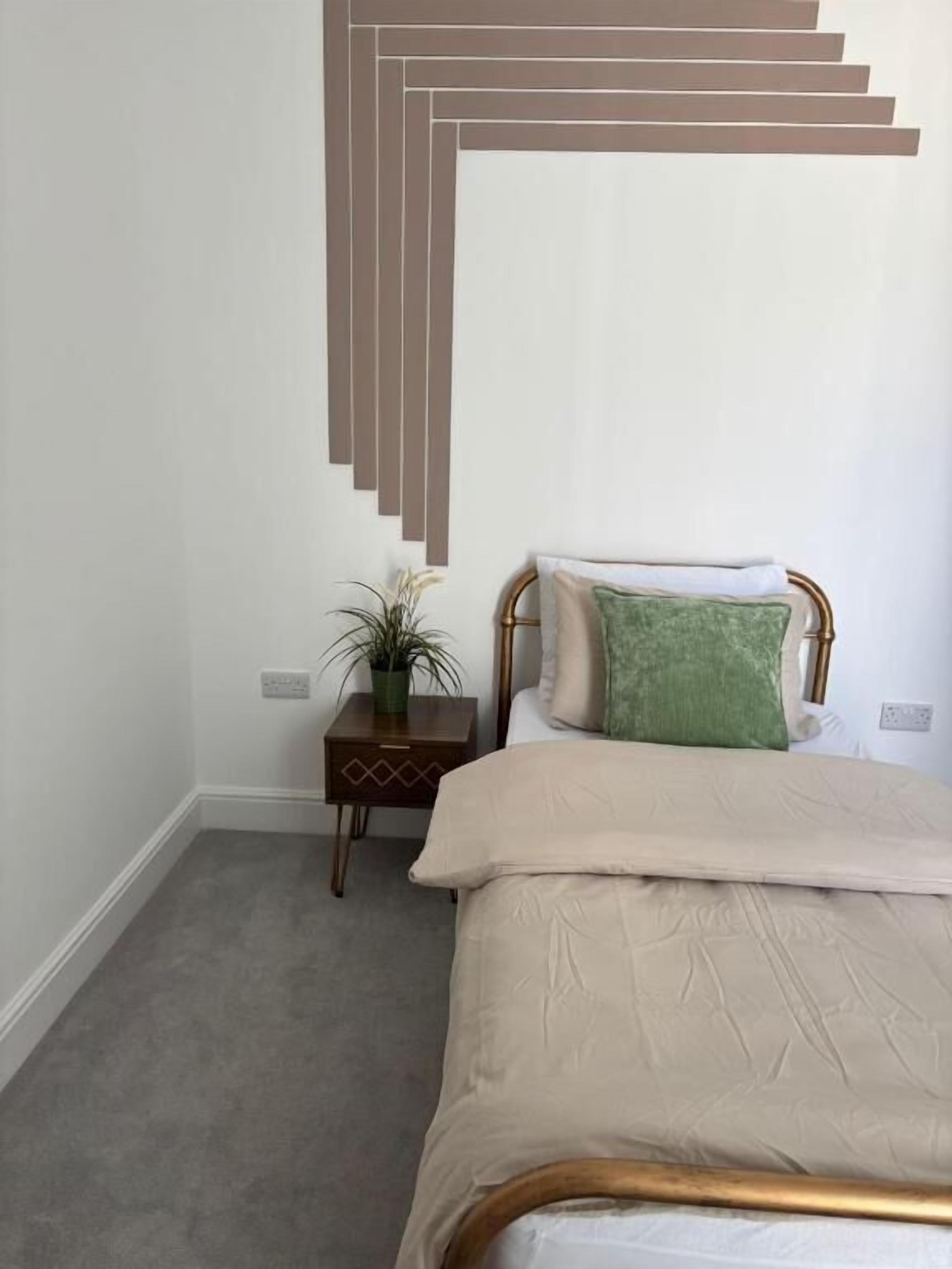 A bedroom with a bed, a nightstand with a plant, and a wall-mounted light fixture.