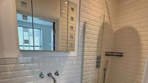 A modern bathroom with a white vanity, a glass shower enclosure, and a large mirror. - Stunning 3 Bed Apartment By Urban Roost (Worthing)