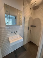 Un baño moderno con tocador blanco, cabina de ducha con vidrio y un espejo grande.