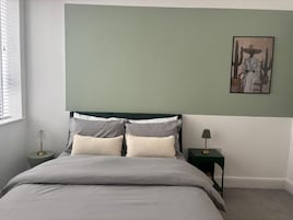 Un dormitorio con una cama, dos mesitas de noche, un velador, una ventana y una obra de arte colgada en la pared.
