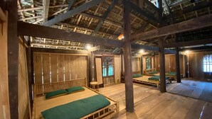 A traditional wooden room with thatched ceilings, multiple beds with green bedding, and a rustic wooden floor.