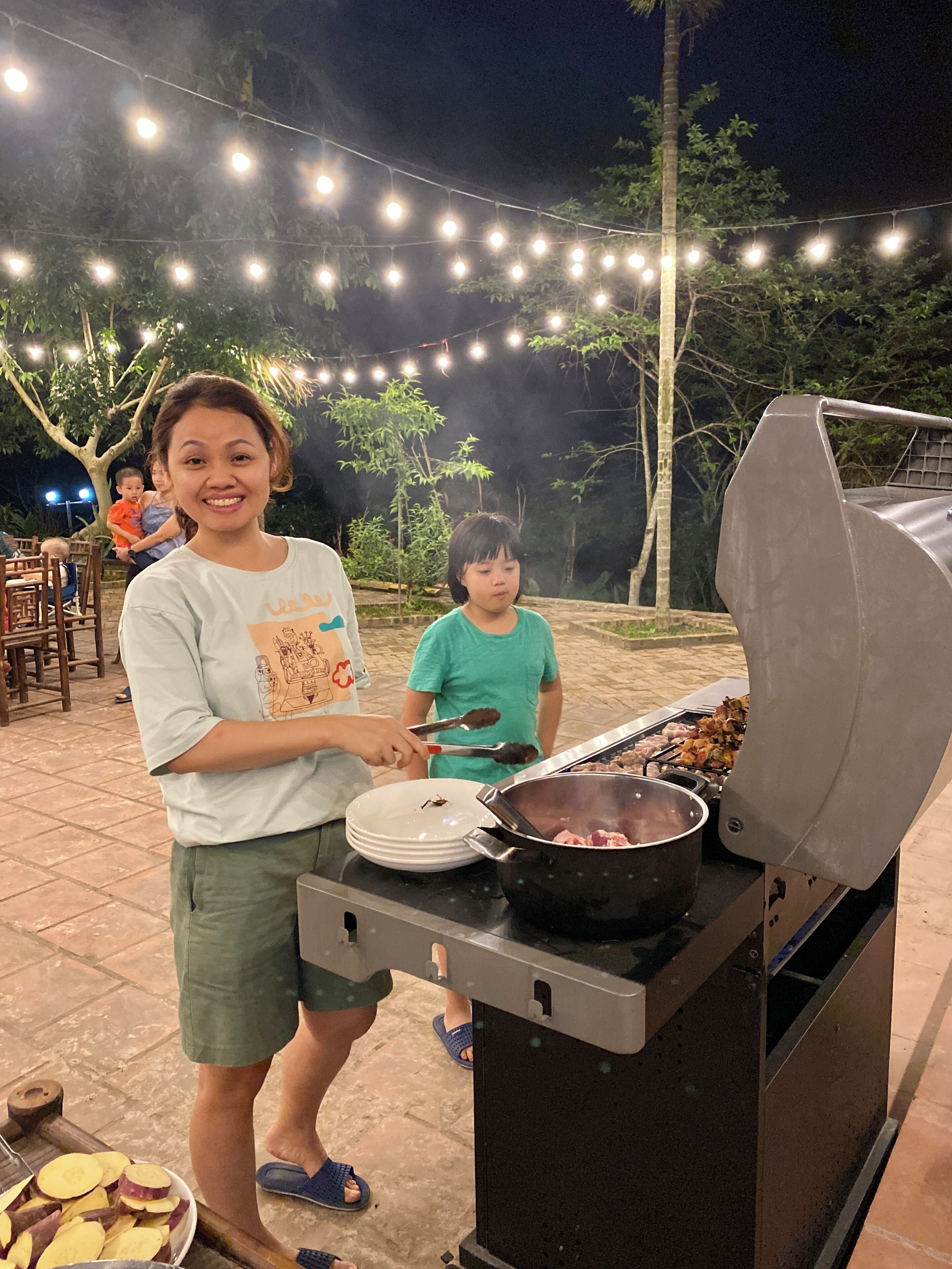 A barbecue grill with skewers, a pot, and sliced vegetables on a table.