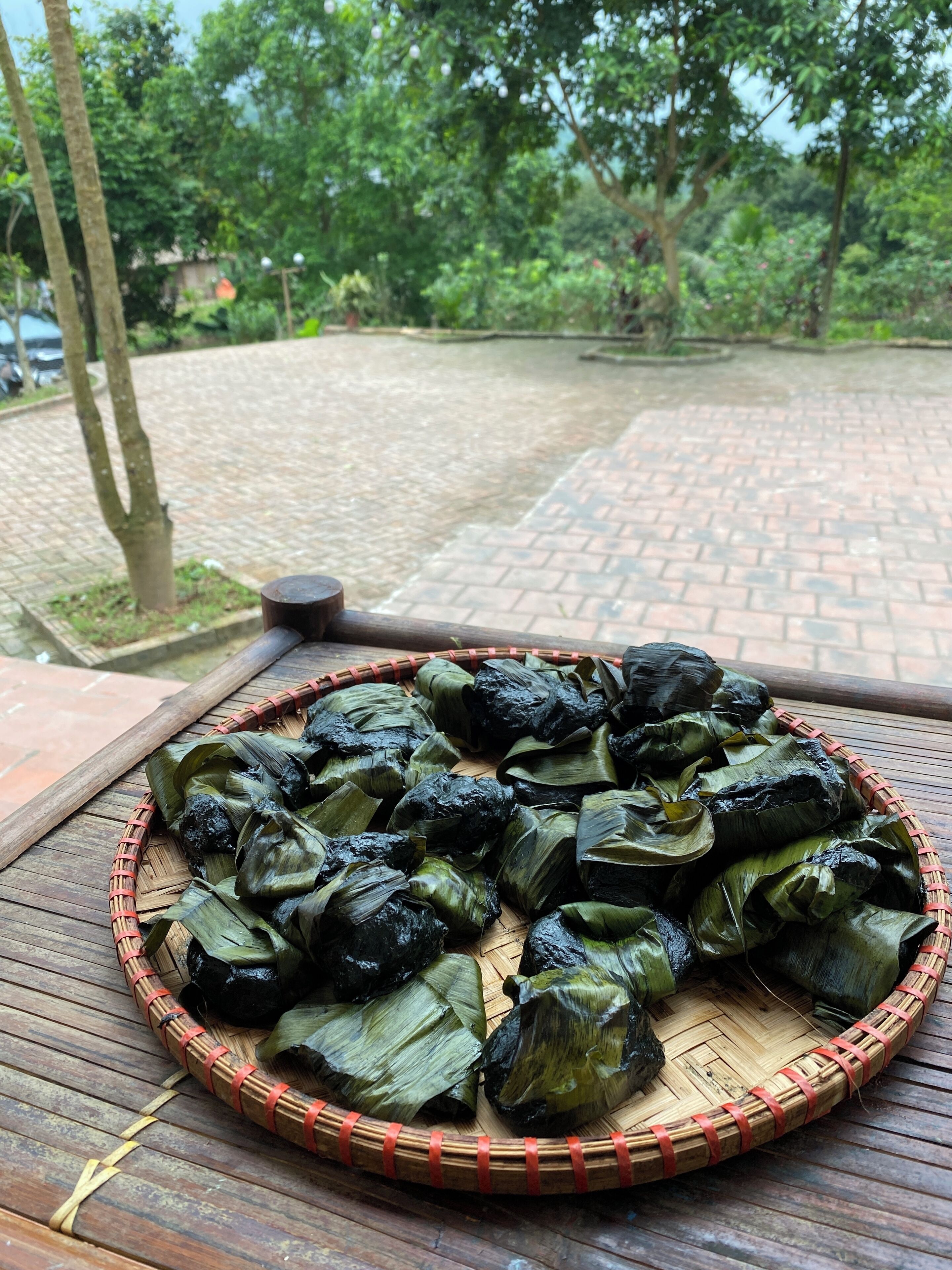 A tray of food items wrapped in leaves, placed on a wooden surface outdoors.