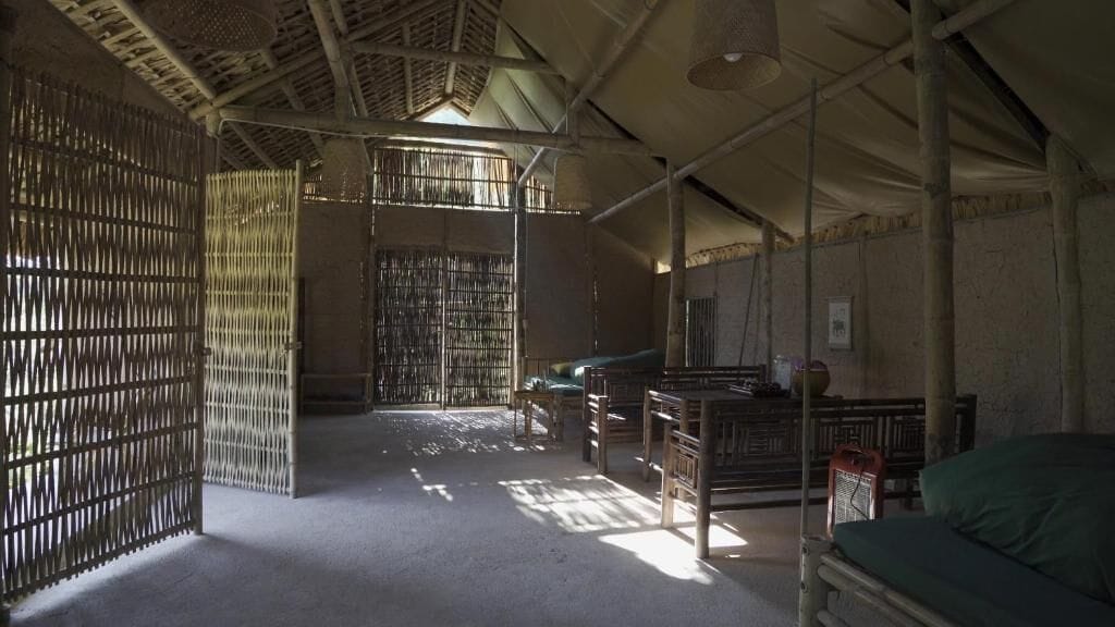 A room with a high ceiling, bamboo partitions, and a bed with a green cover.