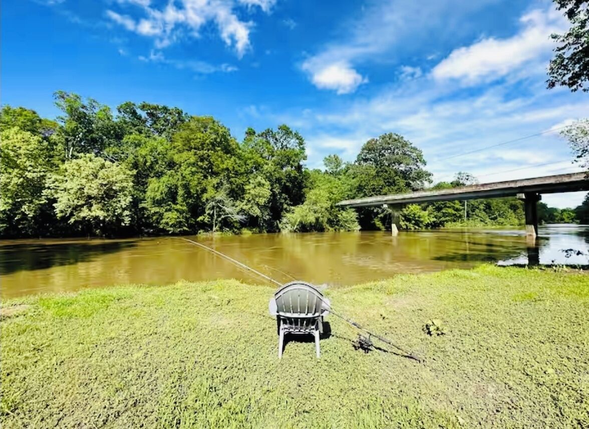 A chair by a river with a bridge in the background.
