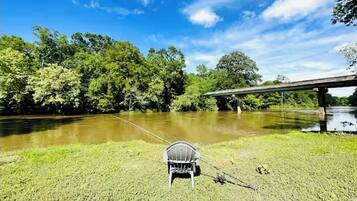 A chair by a river with a bridge in the background.