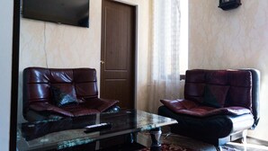 Une pièce comprenant deux canapés en cuir, une table basse en verre, un téléviseur à écran plat et une horloge murale.