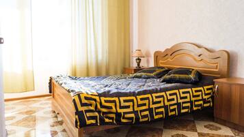 Quarto de hotel com cama, mesa de cabeceira, abajur e janela com cortinas.