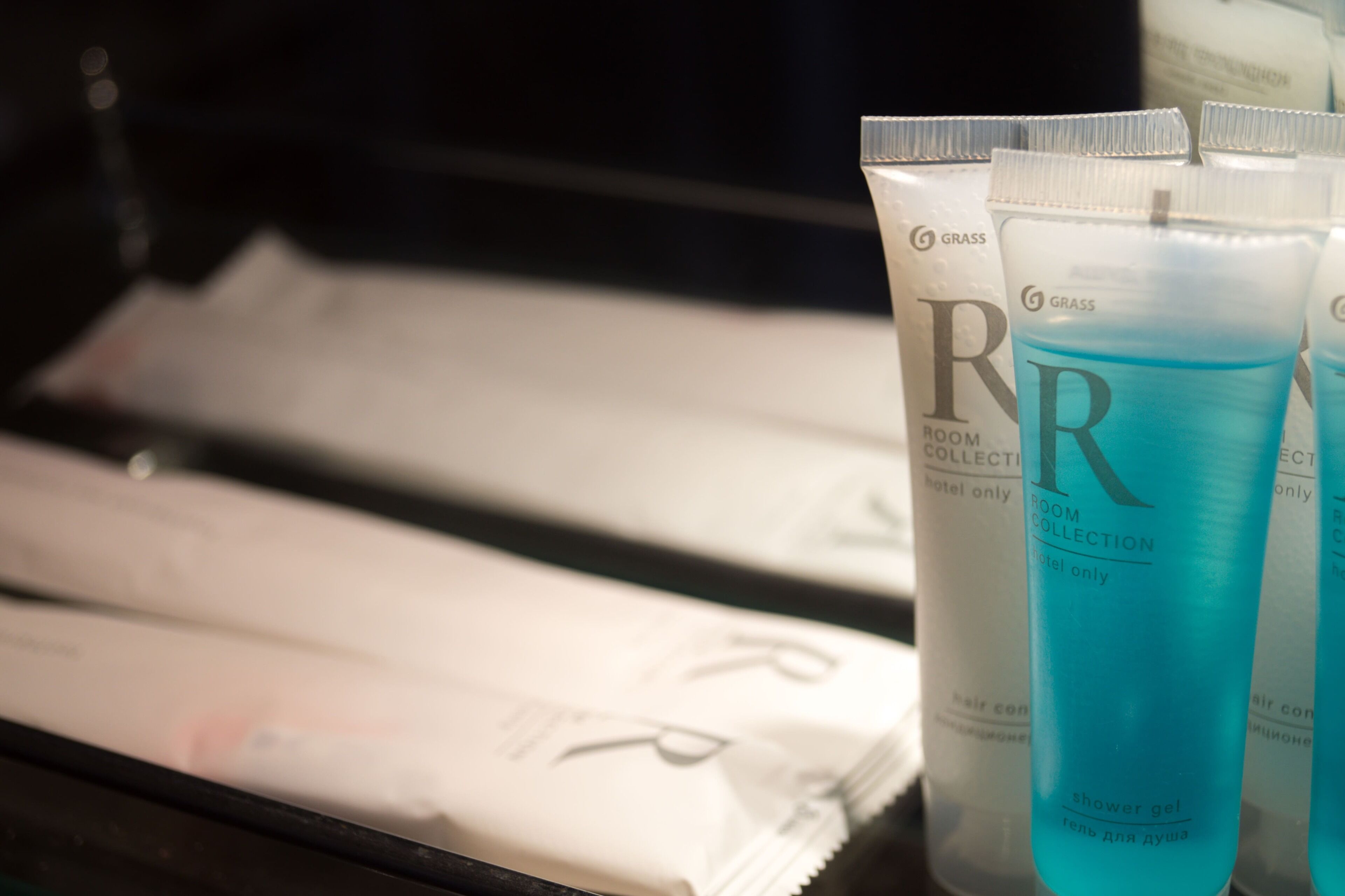 A display of hotel toiletries including a blue shower gel bottle, a white tube labeled 'ROOM COLLECTION hotel only,' and a white tube with 'GRASS' branding.