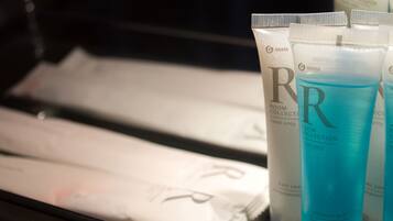 A display of hotel toiletries including a blue shower gel bottle, a white tube labeled 'ROOM COLLECTION hotel only,' and a white tube with 'GRASS' branding.