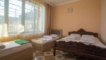 A room with two beds, a wooden headboard, a nightstand, and a window with curtains.