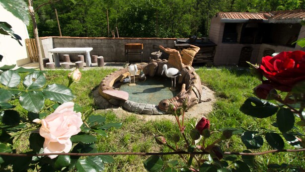 Un jardin agrémenté d’un foyer extérieur en pierre, d’un espace salon et d’un petit bâtiment doté d’un toit en tuiles.