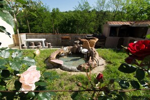 Un jardín con un hogar de piedra, una zona de estar y un pequeño edificio con tejado de azulejos.