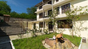Un immeuble de deux étages doté d’un balcon au deuxième étage, d’un escalier menant à l’entrée et d’un petit jardin agrémenté d’une statue.