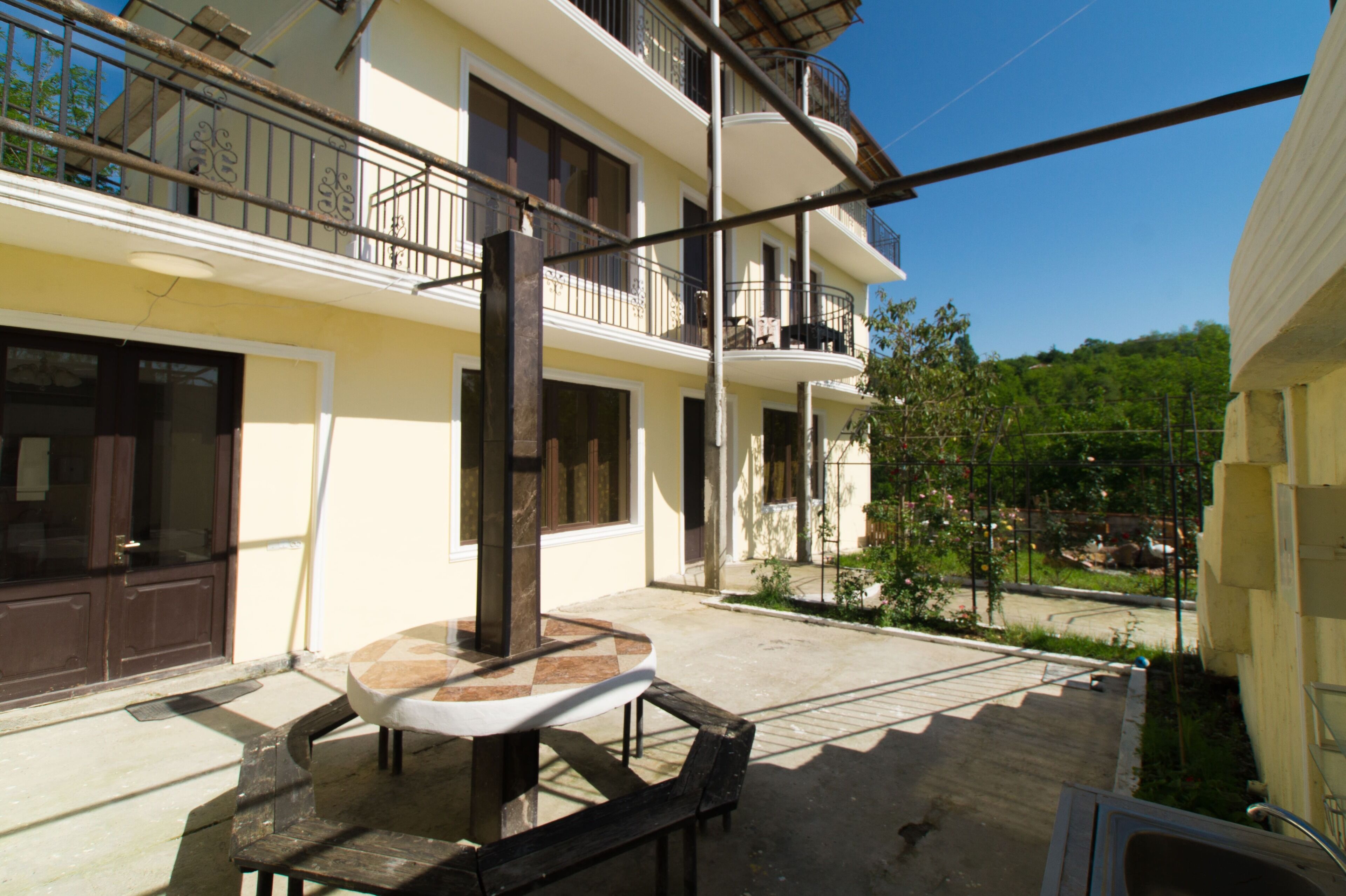 Un edificio de varios pisos con balcones, un patio con mesa y sillas, y vistas al entorno verdeado.