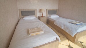 Une chambre avec deux lits simples, chacun doté d’une tête de lit en bois et d’une table de chevet avec une lampe.