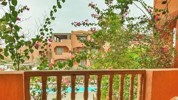 A balcony with wicker chairs, a fruit bowl, and a view of a swimming pool and buildings.