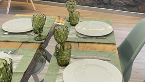 A dining area with a stone wall backdrop, a blue upholstered chair, and a table set with green glassware and white plates. - Raízes AL-House with stunning sea views in Povoação, São Miguel, Azores. (Açores)