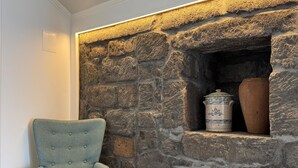 A room with a stone fireplace, a blue upholstered armchair, and a wooden floor. - Raízes AL-House with stunning sea views in Povoação, São Miguel, Azores. (Açores)