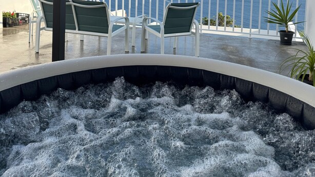A hot tub with a view of the ocean, outdoor seating, and a white railing. - Raízes AL-House with stunning sea views in Povoação, São Miguel, Azores. (Açores)