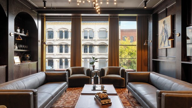 A modern lounge with leather sofas, a coffee table, and a view of a classical building. - The Reserve on Main (Louisville)