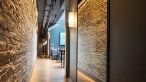 A narrow corridor with exposed brick walls, wooden flooring, and a seating area with tables and chairs. - The Reserve on Main (Louisville)