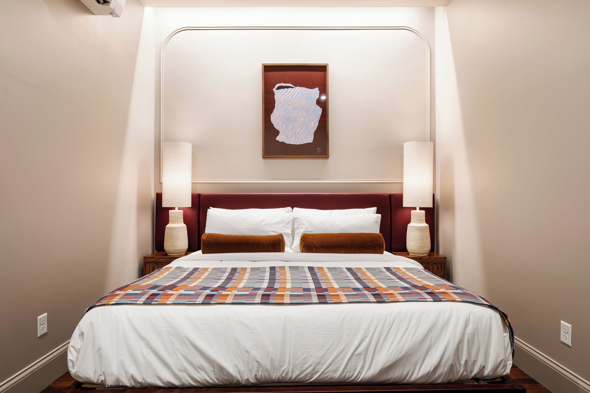 A hotel room with a large bed, two bedside lamps, a headboard with a map artwork, and a quilt.