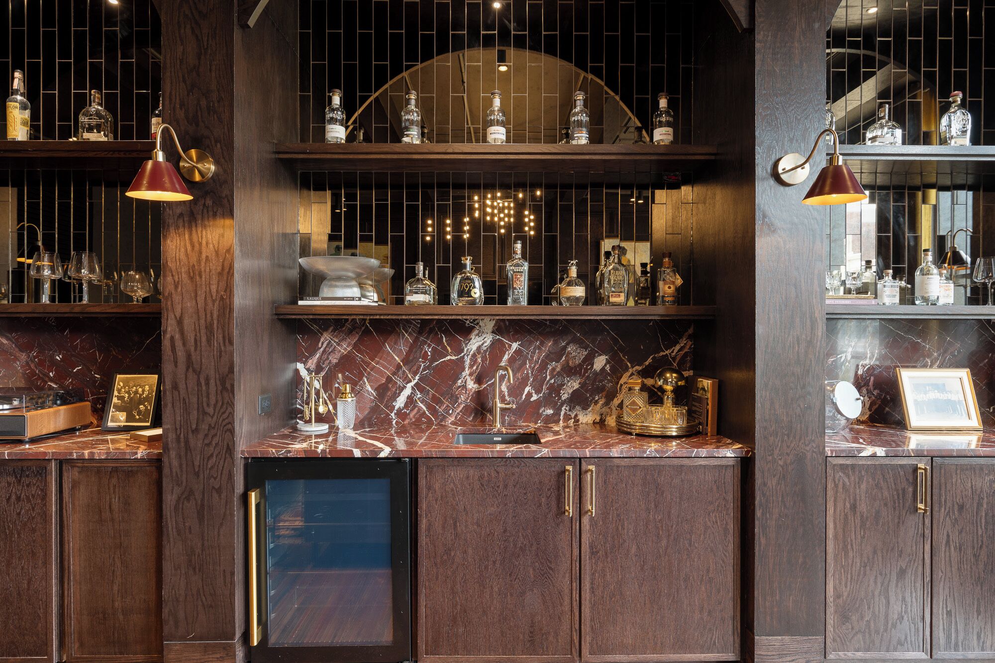 A bar area with marble countertops, wooden cabinets, and shelves displaying liquor bottles.