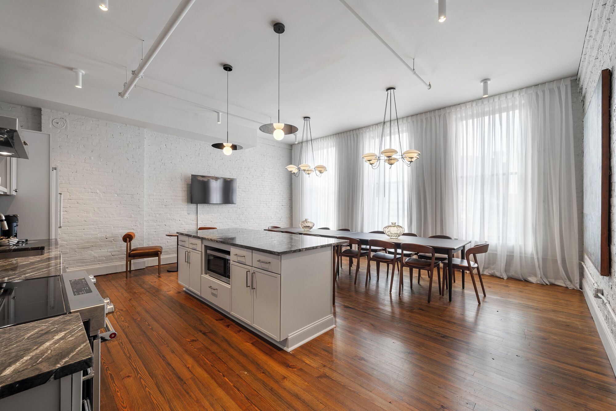A modern kitchen with a central island, wooden flooring, and pendant lighting.
