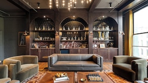 A modern living room with a leather sofa, two coffee tables, and a chessboard. There are shelves with bottles and glasses, and a large window on the right. - The Reserve on Main (Louisville)