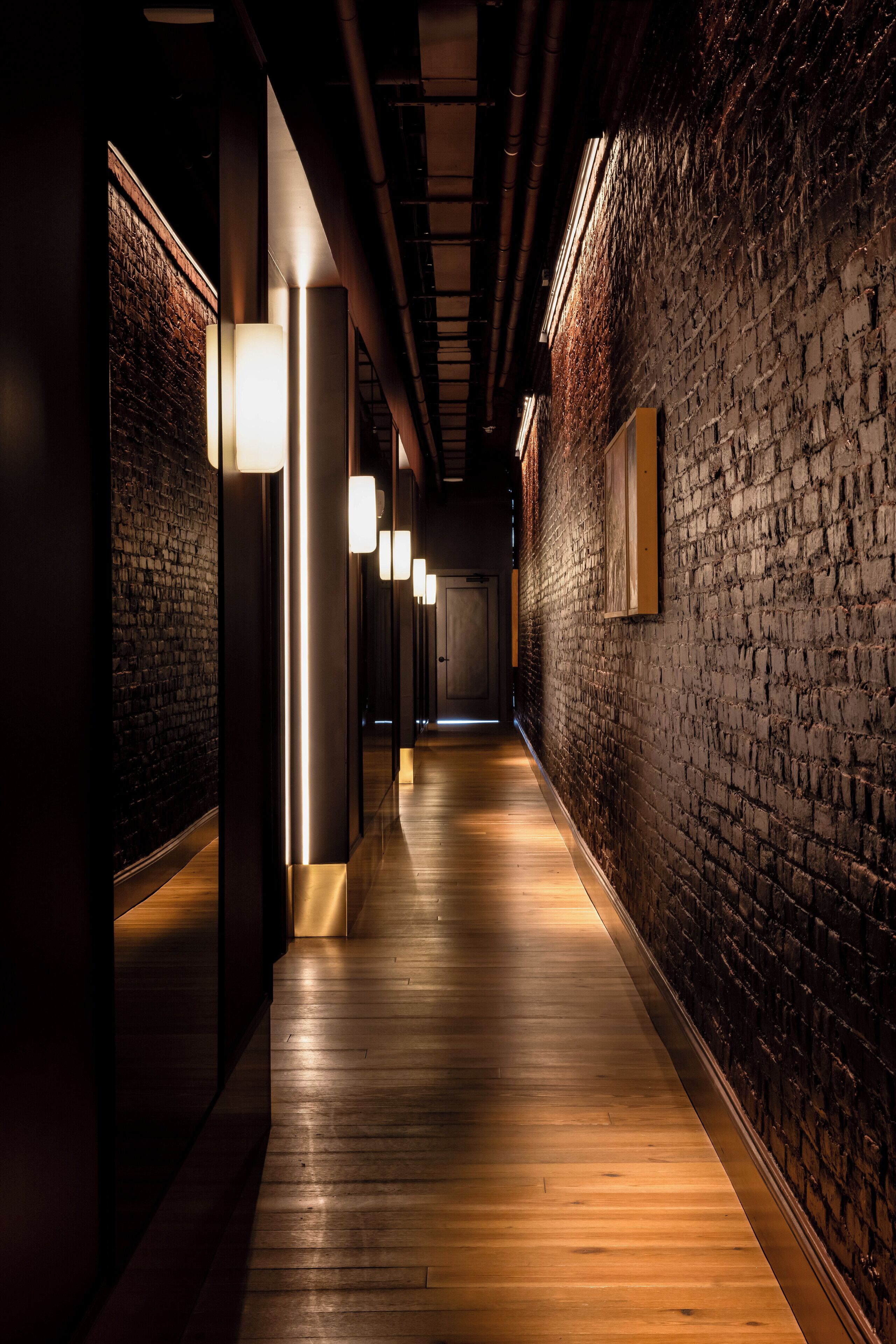 A corridor with wooden flooring, brick walls, and modern lighting fixtures.