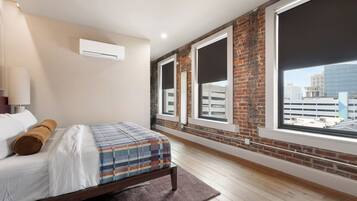 A bedroom with a bed, a large window, and a view of the city.