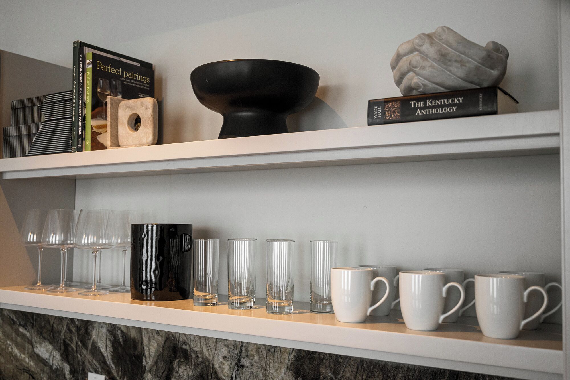 A shelf with books, a black bowl, and a sculpture.