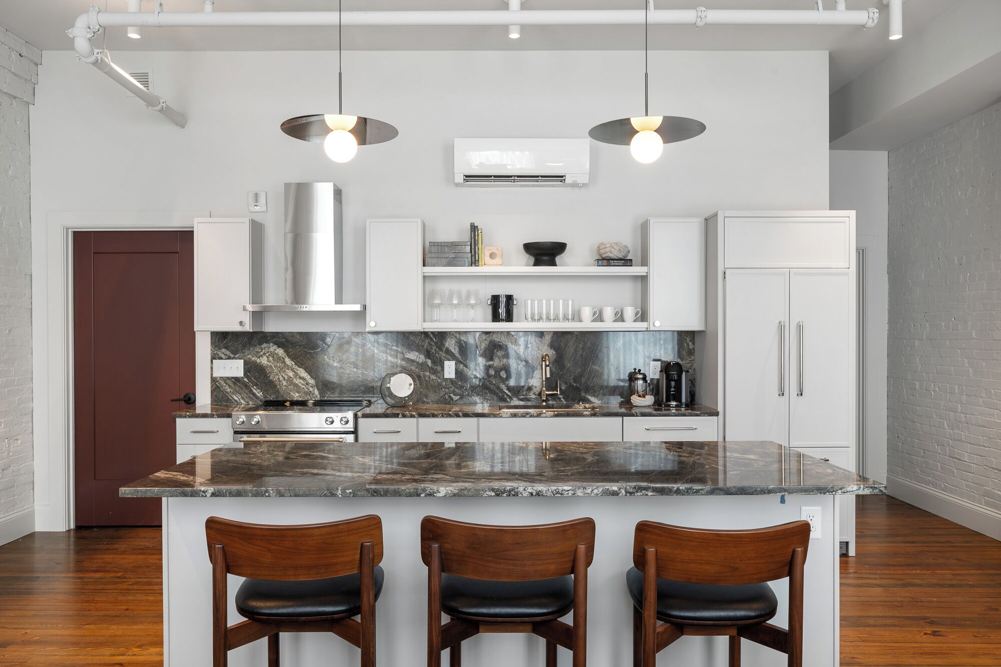 A modern kitchen with a marble countertop, stainless steel appliances, and a central island with bar stools.