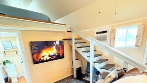 A living room with a large TV mounted on the wall, a staircase, and a patterned rug.