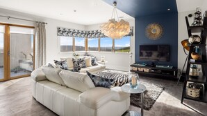 A modern living room with a white sofa, a large chandelier, and a view of the countryside through the windows. - Suaimhneas Villa with Castle and Sea Views (Clifden)