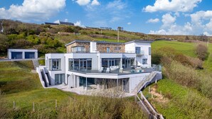 A modern house with a large glass balcony, a stone facade, and a hillside setting. - Suaimhneas Villa with Castle and Sea Views (Clifden)