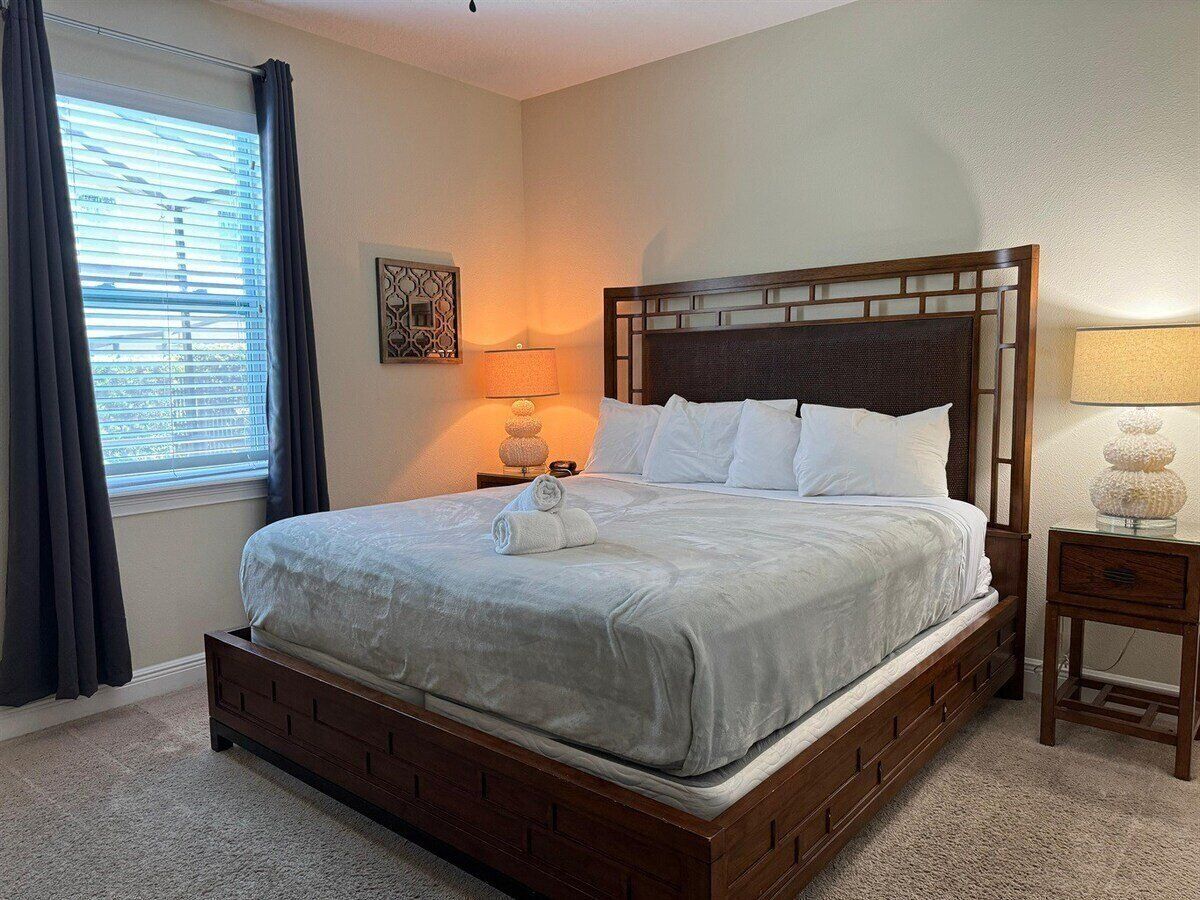 Een opgemaakt bed met een houten hoofdbord, een bedlampje en een decoratief wandobject.