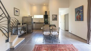 A spacious living area with a kitchen, a dining table with chairs, a staircase, and artwork on the walls. - Architect-designed house for 8 people set in greenery. Near Rambouillet, Paris (Orphin)