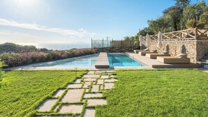 A swimming pool with a stone deck and steps, surrounded by a stone wall and greenery.