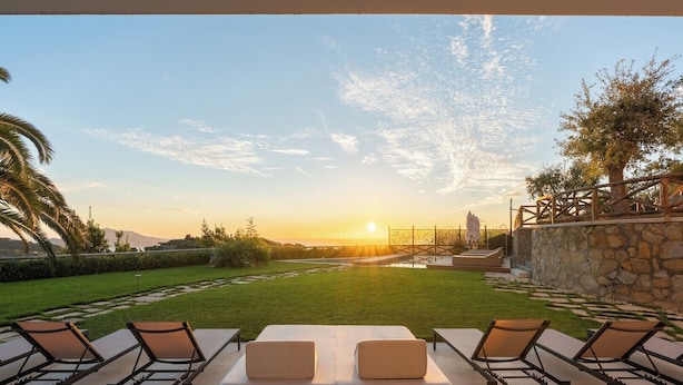 A patio with a sofa and chairs facing a sunset view.