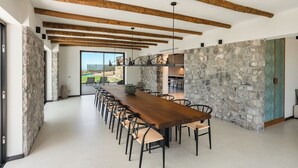 A spacious dining area with a long wooden table and chairs, stone walls, and exposed wooden beams on the ceiling.