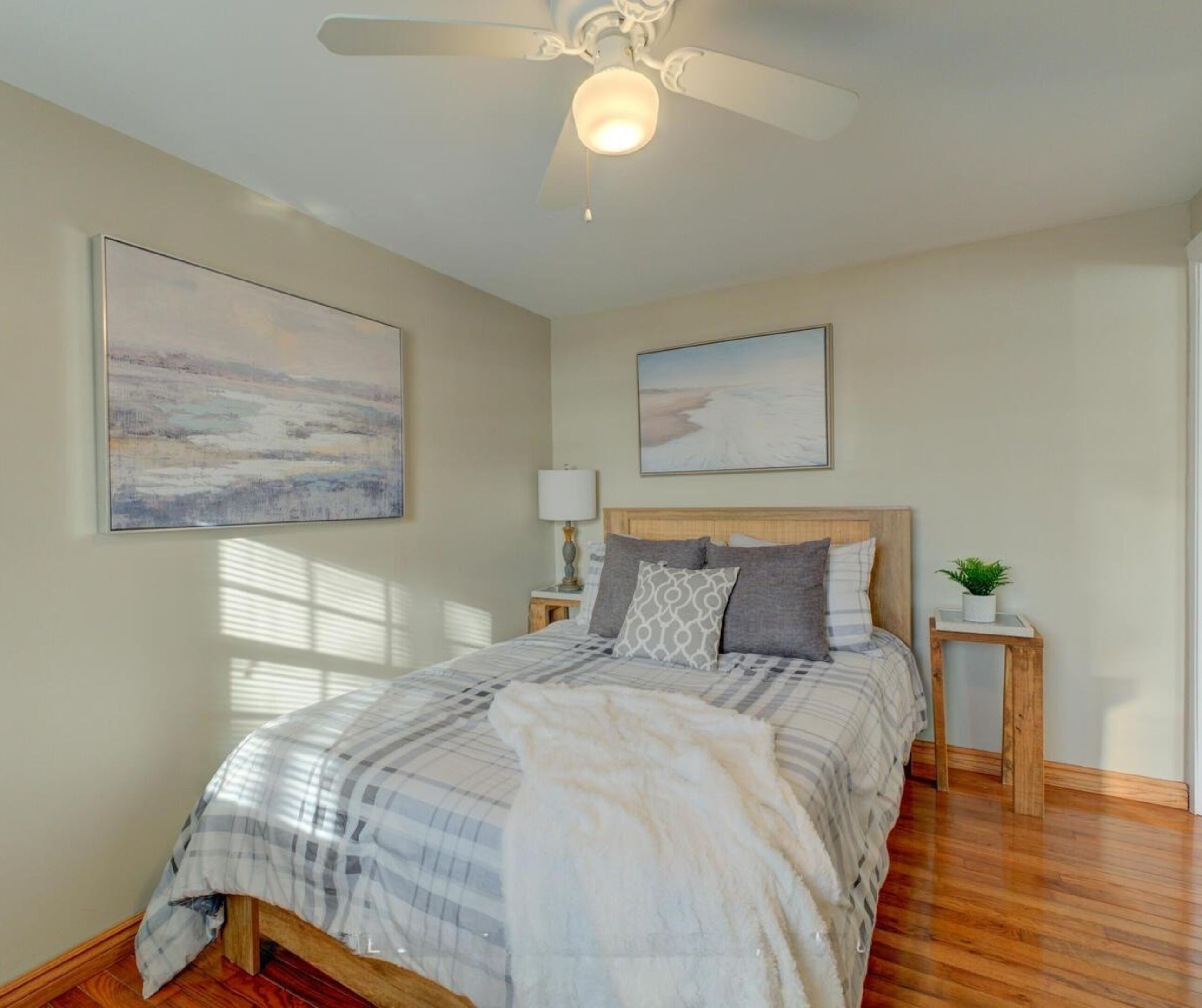 A bedroom with a bed, a ceiling fan, two bedside tables, and two wall-mounted paintings.