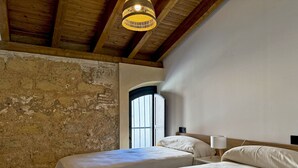 A room with two beds, a rustic brick wall, a wooden ceiling, and a large window. - La Solera de Jerez - Ole Solutions (Jerez de la Frontera)