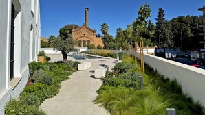 A pathway leading to a building with a brick facade and a tall chimney. - La Solera de Jerez - Ole Solutions (Jerez de la Frontera)