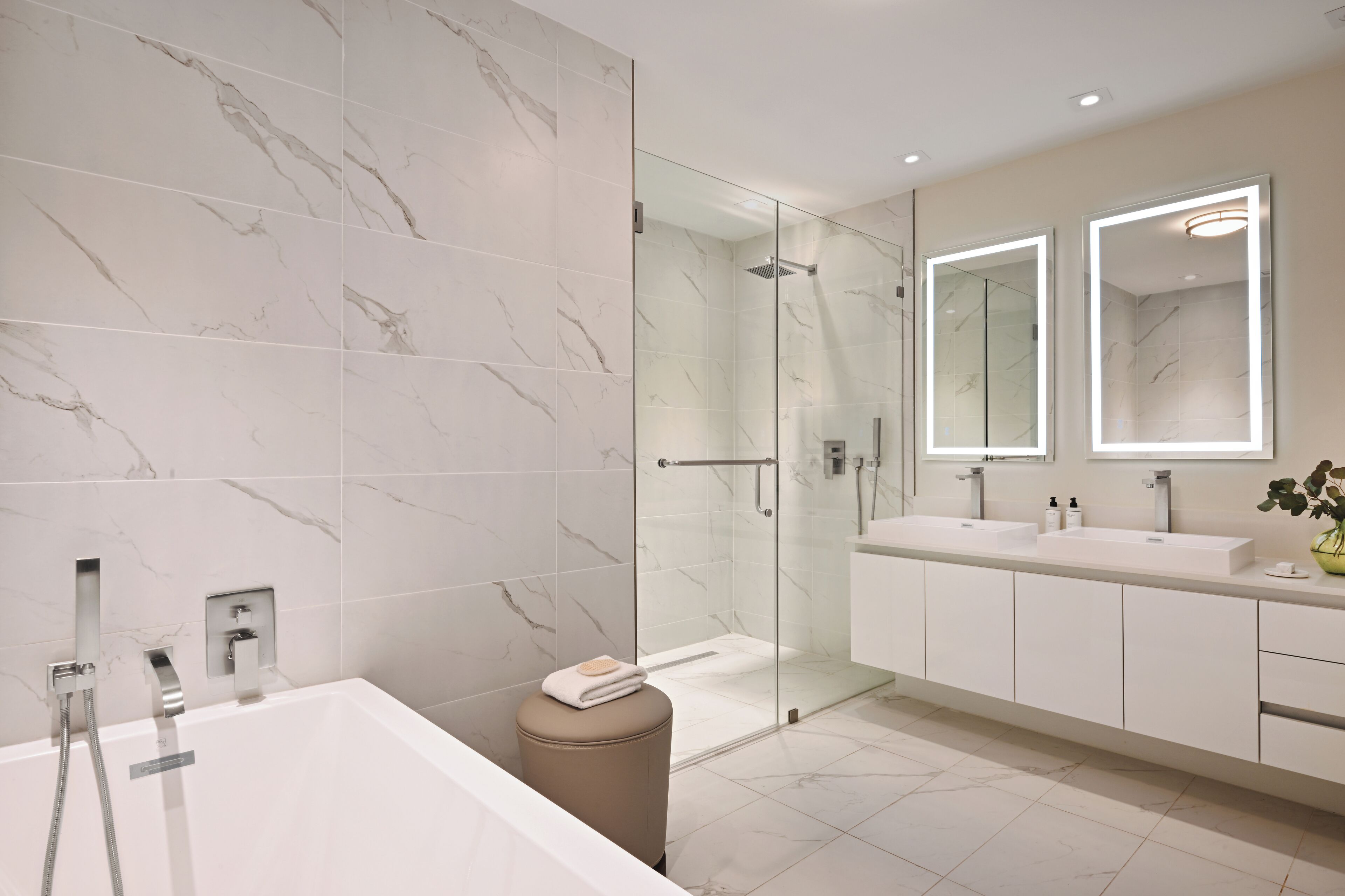 A modern bathroom with a glass-enclosed shower, a bathtub, and a vanity with two mirrors.