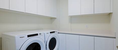 A laundry room with two white Whirlpool washing machines, white cabinets, and a white countertop.